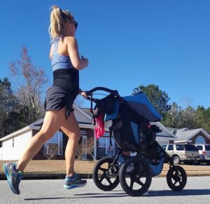 Woman running wearing the Babybellyband Original Pregnancy Band while pushing a stroller